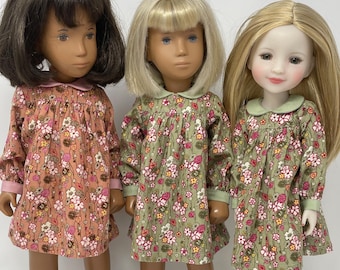 Puede incluir: Tres muñecas con vestidos de estampado floral. La muñeca de la izquierda lleva un vestido rosa con cabello castaño. La muñeca del centro lleva un vestido verde con cabello rubio. La muñeca de la derecha lleva un vestido verde con cabello rubio.