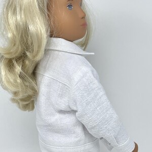 May include: A white doll wearing a white jacket and pants. The jacket has a collar and buttoned cuffs. The doll has blonde hair and blue eyes. The outfit appears to be made of a textured fabric.
