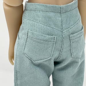 May include: Light sage green corduroy pants featuring a high-waisted design with a structured waistband, two functional back pockets, and visible vertical ribbed texture. The trousers are tailored with a classic yoke seam across the back.