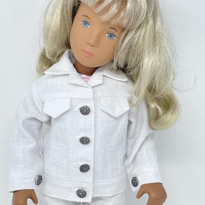 May include: A doll wearing a white jacket and matching pants. The jacket has decorative buttons and pocket flaps. The doll has blonde hair and blue eyes. The outfit is made of a textured fabric.