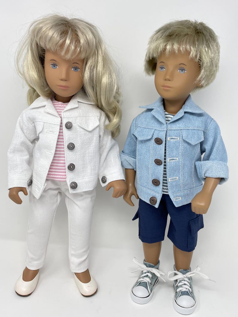 May include: Two dolls dressed in matching outfits. One doll wears a white jacket, pink striped shirt, and white pants. The other doll wears a blue denim jacket, striped shirt, and navy shorts. Both dolls have blonde hair and are wearing shoes.