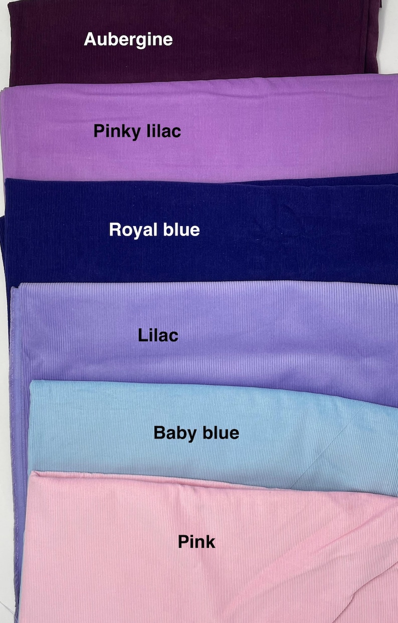 Pu&ograve; includere: Una collezione di sei campioni di tessuto piegati con una consistenza a coste. I colori sono etichettati come Aubergine, Pinky lilac, Royal blue, Lilac, Baby blue e Pink. Ogni pezzo di tessuto &egrave; impilato orizzontalmente, mostrando un colore solido.