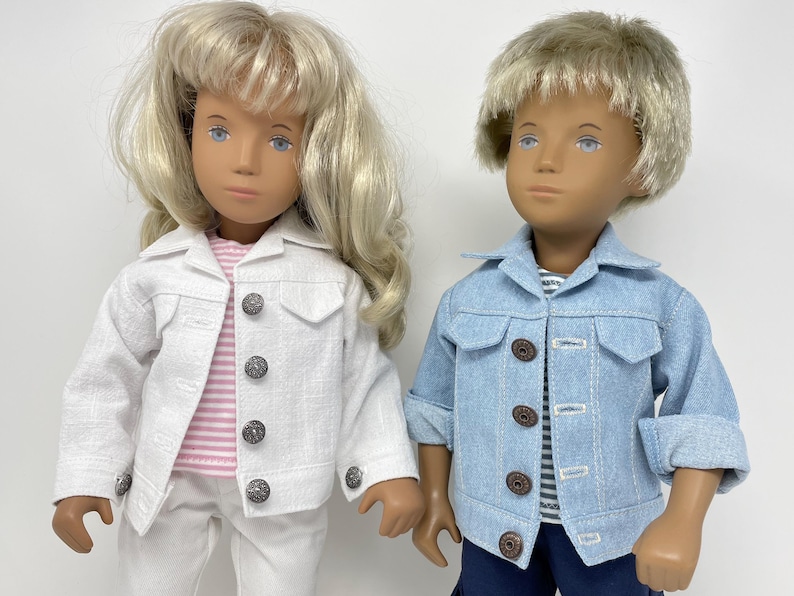 May include: Two dolls are shown, one with blonde hair and the other with short, light brown hair. The doll on the left wears a white jacket, pink striped shirt, and white pants. The doll on the right wears a light blue denim jacket and a striped shirt.