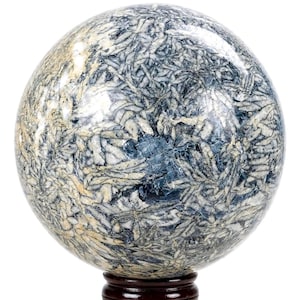 Puede incluir: Una piedra esférica pulida que presenta un patrón complejo en forma de estrella de estructuras cristalinas blancas y gris claro incrustadas en una matriz de color azul profundo y gris carbón, sobre una pequeña base circular de madera oscura.