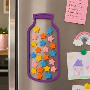 Peut inclure: Un cadre magnétique violet en forme de bocal contenant de nombreux petits aimants en forme d'étoiles aux couleurs jaune, orange, rose et bleu. Le cadre est fixé sur une surface métallique à côté d'une note rose avec le texte Daily Jobs.