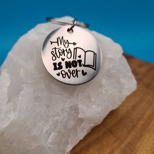 May include: A silver keychain with a round charm that says "My story is not over" with a book and heart symbols.