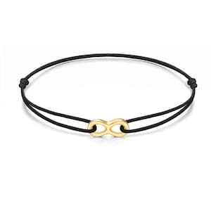 May include: A black cord bracelet featuring a gold-colored infinity symbol charm. The bracelet has a simple design with adjustable knots on each end. The infinity charm is a prominent focal point, adding a touch of elegance.