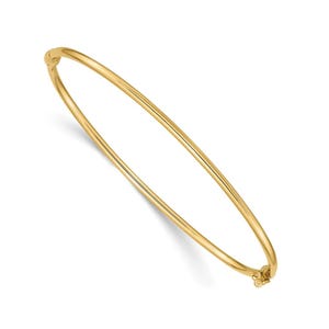 May include: A gold bangle bracelet with a hinged clasp. The bracelet is a simple, elegant design, perfect for everyday wear. The gold has a polished finish, reflecting light. This classic piece of jewelry is a timeless accessory.