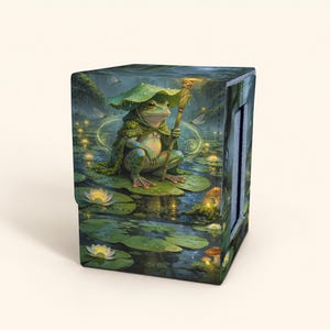 May include: A rectangular deck box featuring a printed illustration of a green frog wearing a leaf hat and cloak, holding a wooden staff while sitting on a lily pad in a pond with white water lilies, mushrooms, and glowing fireflies.