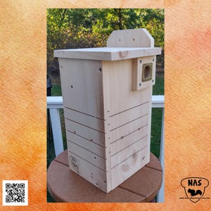 May include: A natural wood birdhouse with a rectangular shape and a small roof. The birdhouse has a circular entrance and horizontal grooves on the front. The birdhouse is made of light-colored wood and is designed for outdoor use.