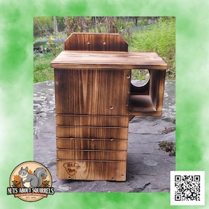 May include: A wooden squirrel house with a natural, burnt finish. The house features a main compartment with a series of horizontal slats and a side entrance. The top has a small roof-like structure. The logo "Nuts About Squirrels" is visible.
