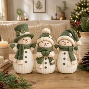 May include: Three decorative snowman figurines with off-white bodies and ribbed textures. Each wears a green knitted hat and scarf with cream-colored accents. The snowmen feature orange carrot noses, black eyes, and green buttons on their torsos.