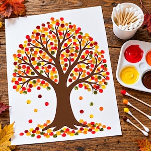 May include: A white sheet of paper featuring a brown tree trunk and branches with colourful circular paint dots in red, orange, yellow, and green representing autumn leaves. A paint palette with four colours and a cup of cotton swabs are nearby.
