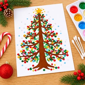 Op de afbeelding: Een wit vel papier met een bruine, handgeschilderde kerstboom met kleurrijke stippen als versiering en een gele ster op de top. Het kunstwerk is omringd door een zuurstok, een rode kerstbal, dennentakken, een dennenappel, verf en wattenstaafjes.