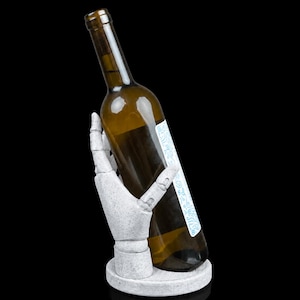May include: A white, speckled, articulated hand sculpture mounted on a circular base, gripping a brown glass wine bottle. The bottle features a white label with blue decorative line art patterns. The entire object is set against a black background.