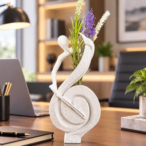 May include: A white speckled abstract sculpture vase featuring a stylized human figure leaning against a curved, spiral-shaped base. The sculpture holds a collection of artificial white and purple floral stems extending upward from the center.
