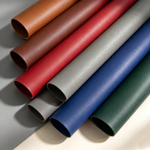 May include: A collection of rolled sheets of faux leather in various colors including tan, brown, red, gray, blue, and dark green. Each roll features a consistent textured surface and a hollow cylindrical shape, arranged in a diagonal pattern.