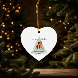 K&ouml;nnte beinhalten: Ein wei&szlig;er herzf&ouml;rmiger Keramikschmuck, der an einer goldenen Schnur h&auml;ngt. In der Mitte befindet sich eine Grafik eines Babys in roter Kleidung in einem stilisierten Weihnachtsbaum mit dem Text Anaya Smith's First Christmas 2019.