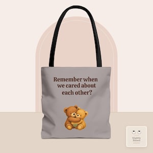 May include: A light gray tote bag with black handles featuring a brown illustration of two teddy bears hugging. The text "Remember when we cared about each other?" is printed in brown above the bears. A small square logo with eyes is in the corner.