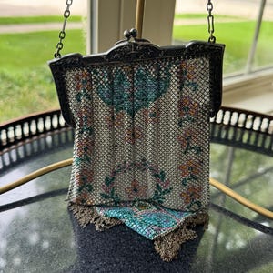 May include: A vintage metal mesh handbag featuring a floral pattern in shades of turquoise, pink, and orange on a white background. The bag has an ornate silver-toned metal frame with a kiss-lock closure and a delicate chain strap with fringe.