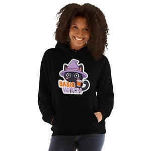 Può includere: Una felpa nera con cappuccio caratterizzata da una grafica di un gatto nero che indossa un cappello da strega viola e tiene in mano una tazza di caffè. Il testo "BASIC WITCH" è stampato in lettere arancioni e viola sotto il gatto dagli occhi a stella.