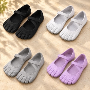 May include: Four pairs of five-toe shoes in black, white, gray, and light purple. Each pair features a rounded toe box with individual toe compartments, a low-cut opening, and a single adjustable hook-and-loop strap across the top of the foot.