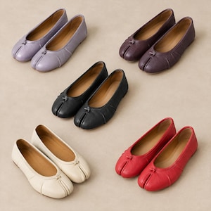 May include: Five pairs of split-toe ballet flats arranged in a circular pattern. The shoes are available in lavender, dark purple, black, cream, and red. Each pair features a small decorative knot detail at the center of the toe box and a low heel.