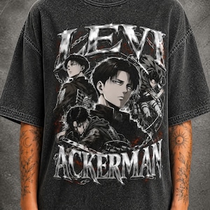 May include: A charcoal gray acid-wash t-shirt featuring a graphic print of the anime character Levi Ackerman. The design includes the text LEVI ACKERMAN in a metallic silver font, with multiple illustrations of the character in combat gear.