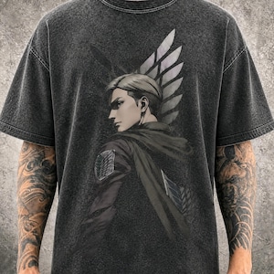 May include: A charcoal grey acid-wash t-shirt featuring a graphic print of a blonde anime character in a dark cloak. The character is shown in profile with a wing emblem visible on the shoulder and a large wing design in the background.