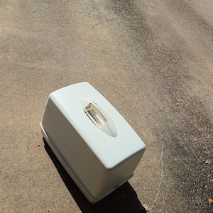 May include: A rectangular white plastic sewing machine carrying case with a smooth, solid exterior and a central, integrated handle on the top surface. The case features rounded corners and a clean, simple design for storage and transport.