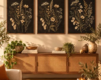 Könnte beinhalten: Drei rechteckige Wandbilder mit gepressten botanischen Arrangements aus Wildblumen und Gräsern in Creme-, Gold- und Grüntönen auf schwarzem Hintergrund, jeweils eingefasst in einen schmalen Rahmen aus dunklem Holz.