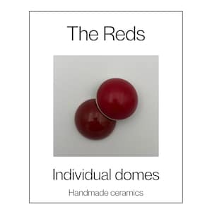 May include: Two smooth, glossy ceramic domes in distinct shades of red. One dome is a bright, vibrant red, while the other is a deeper, darker burgundy red. The text "The Reds", "Individual domes", and "Handmade ceramics" appears on the image.