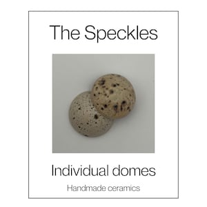 Op de afbeelding: Twee keramische koepels met een gespikkeld patroon, met donkerbruine vlekken op een lichtbeige oppervlak. De tekst "The Speckles", "Individual domes" en "Handmade ceramics" is in het zwart gedrukt op de witte achtergrond rond de objecten.