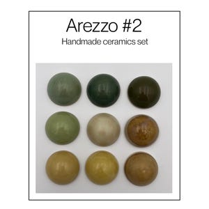 May include: A set of nine round, smooth ceramic pieces arranged in a three-by-three grid, labelled Arezzo #2 Handmade ceramics set. The pieces feature a variety of glossy, earthy tones including shades of sage green, dark forest green, olive, beige, and brown.