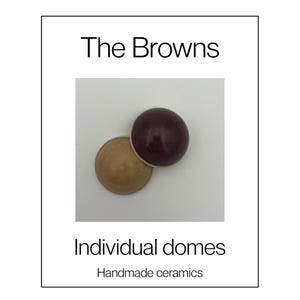 Op de afbeelding: Twee gladde, halfronde keramische koepels, één in donkerbordeaux en de andere in een gedempt beige, worden samen getoond. De tekst "The Browns", "Individual domes" en "Handmade ceramics" staat in zwarte letters op een witte achtergrond.