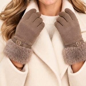 May include: A pair of taupe suede-textured gloves featuring a decorative strap with a gold-toned metal buckle across the wrist and a plush, fuzzy faux fur cuff at the opening. The gloves have a smooth finish and are designed to cover the hands.