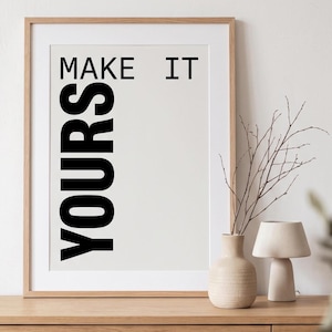 以下が含まれることがあります： 薄いクリーム色の背景に、黒い文字で「MAKE IT」が縦に並び、「YOURS」という単語が大きなサンセリフ体で書かれた額装アートプリント。プリントは明るい色の木製フレームに収められています。