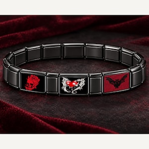 May include: A black modular link bracelet featuring three decorative rectangular tiles. The first tile displays a red skull and rose, the second shows a red heart with silver wings, and the third depicts a black bat on a red background.