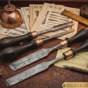 May include: A collection of four vintage steel wood chisels with dark wooden handles and copper ferrules, arranged on a surface with antique H.S.B. & Co. paper catalogues, a wooden ruler, a copper oiler, an inkwell, and a fountain pen.