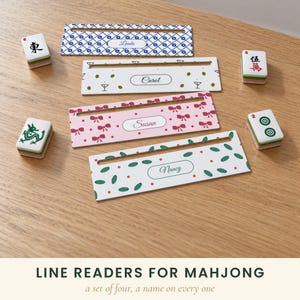 May include: A set of four rectangular mahjong tile holders featuring horizontal slots. Each holder displays a unique pattern and a personalized name: Linda in blue, Carol with olive icons, Susan with pink bows, and Nancy with green leaves.