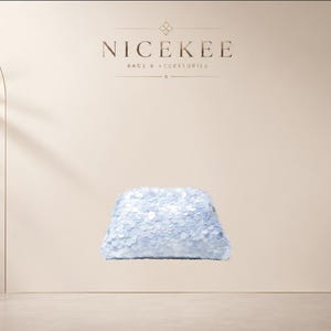 Peut inclure: Une pochette bleu clair recouverte de petites paillettes circulaires réfléchissantes. Le sac présente une forme rectangulaire structurée aux coins arrondis et une texture de surface lisse et scintillante qui capte la lumière.