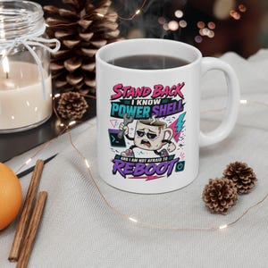 May include: A white ceramic mug featuring a graphic of a cartoon coffee cup wearing sunglasses and holding a wrench. The text reads: STAND BACK I KNOW POWER SHELL AND I AM NOT AFRAID TO REBOOT. The design includes colorful accents and a power button icon.