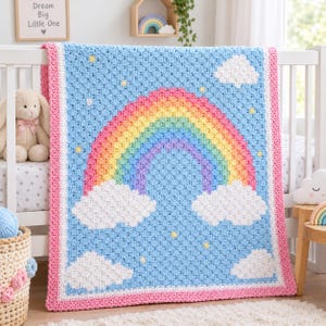 May include: A rectangular crochet blanket featuring a light blue background with a central rainbow in red, orange, yellow, green, blue, and purple. The design includes white clouds at the base of the rainbow and small yellow stars.