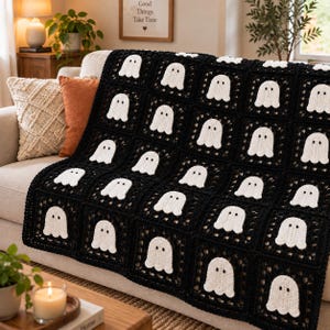 May include: A handmade crochet blanket featuring a repeating pattern of white ghost motifs centered within individual black square blocks. The blanket is constructed from multiple joined squares, each displaying a single ghost with two black eyes.