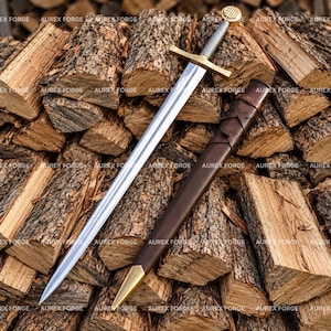 May include: A steel sword with a metallic silver blade, a brass crossguard, and a textured silver grip topped with a circular brass pommel. Beside the sword lies a dark brown leather scabbard featuring a brass tip and cross-laced details.