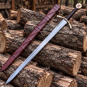 May include: A steel sword with a dark brown leather-wrapped grip, a brass crossguard, and a pommel featuring a red lion emblem. The sword includes a matching dark brown leather scabbard with a crisscross pattern and brass suspension rings.