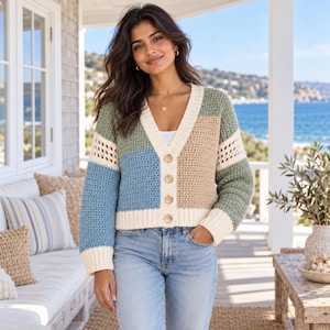 Puede incluir: Un cárdigan con cuello en V y diseño de bloques de color en tonos verde salvia, azul claro y beige. La prenda cuenta con mangas largas con puños acanalados en color crema, un dobladillo acanalado a juego y cierre frontal con cuatro botones marrones.