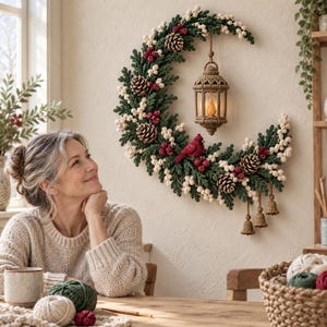 May include: A crescent-shaped wall wreath crafted from green crocheted foliage, white berries, and brown pinecones. A crocheted lantern hangs from the top, while a red cardinal and three small crocheted bells decorate the lower section.