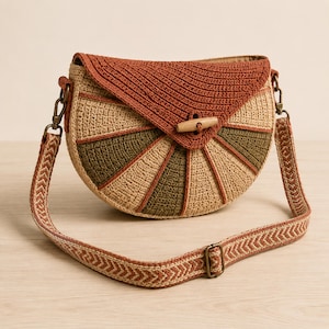 May include: A semi-circular crochet crossbody bag featuring a rust-colored flap with a wooden toggle closure. The body displays a radial pattern of alternating beige and olive green panels. It includes an adjustable woven strap with a chevron pattern.
