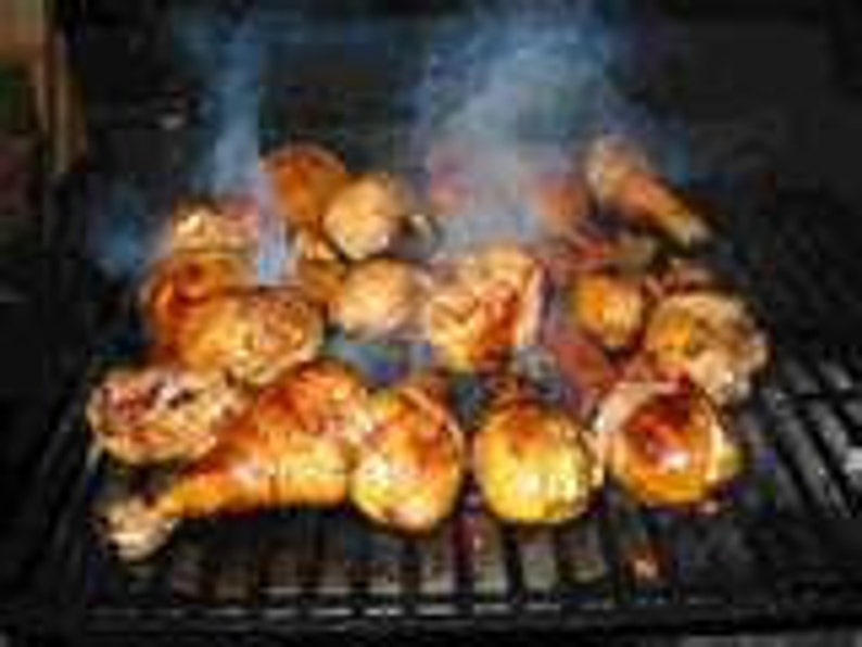 May include: A collection of golden-brown grilled chicken drumsticks and thighs arranged on a black metal barbecue grate. Wisps of white smoke rise from the seasoned poultry as it cooks over the heat, showing charred grill marks on the skin.